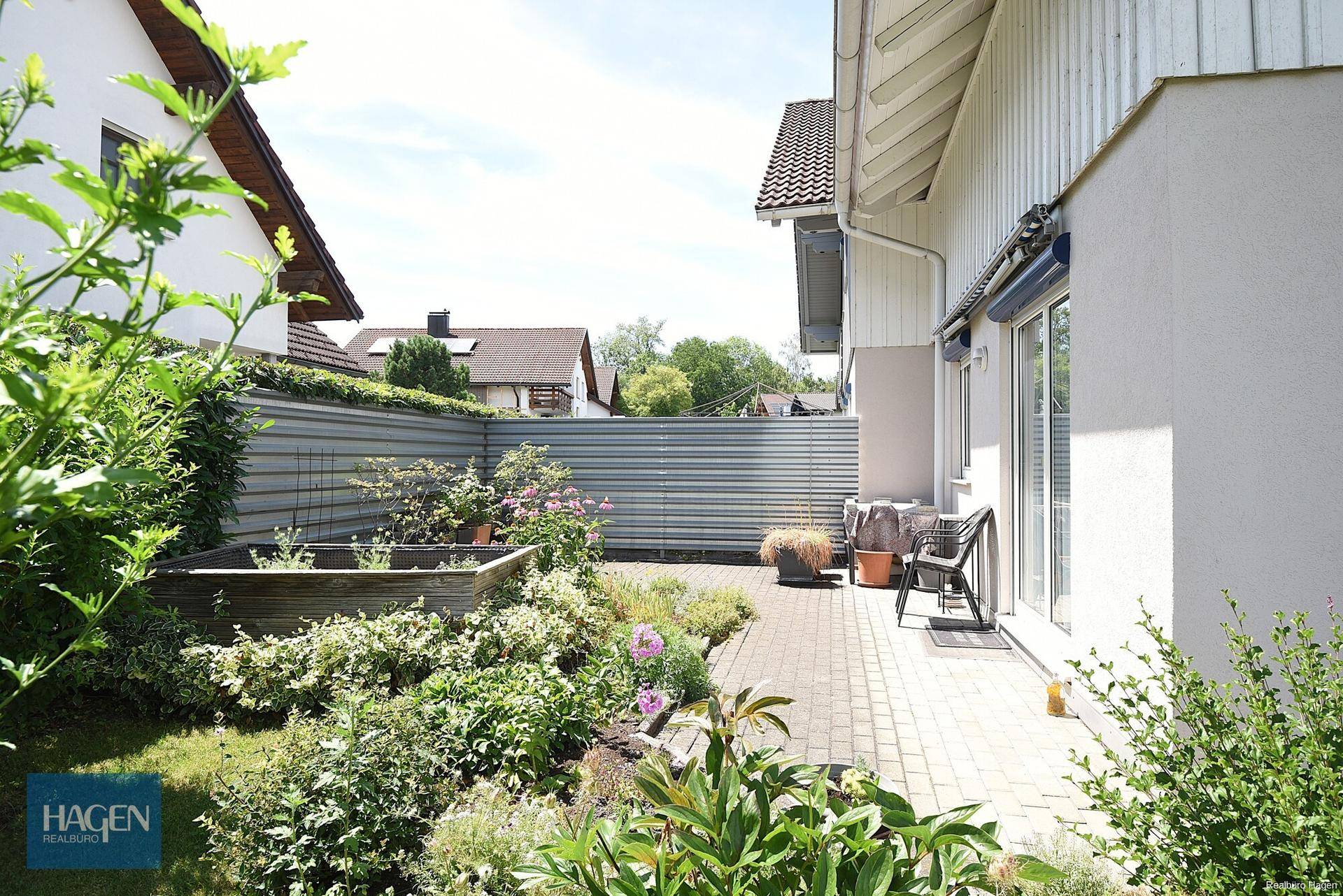 Gepflegter Gartenbereich mit kleiner gepflasterter Terrasse, Hochbeet und Sitzgelegenheiten im Freien.