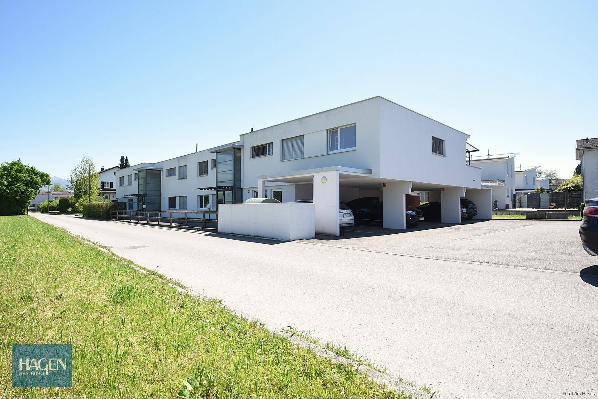 Moderne Wohnanlage mit Flachdach und Carport-Parkplätzen in grüner Umgebung.