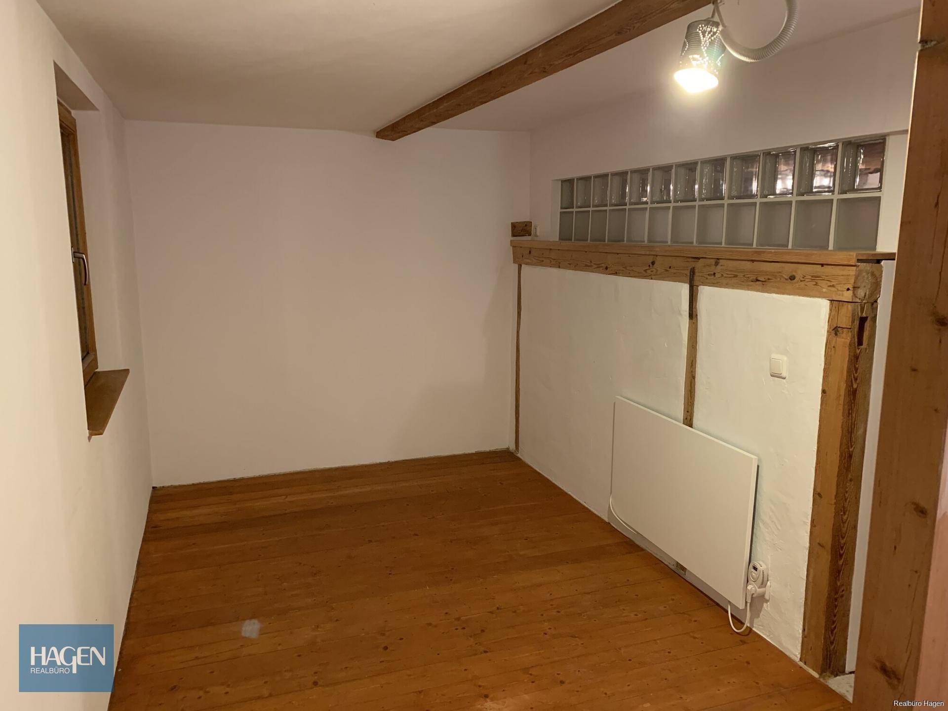 Heller Raum mit Holzboden, weiß gestrichenen Wänden und einem sichtbaren Deckenbalken.
