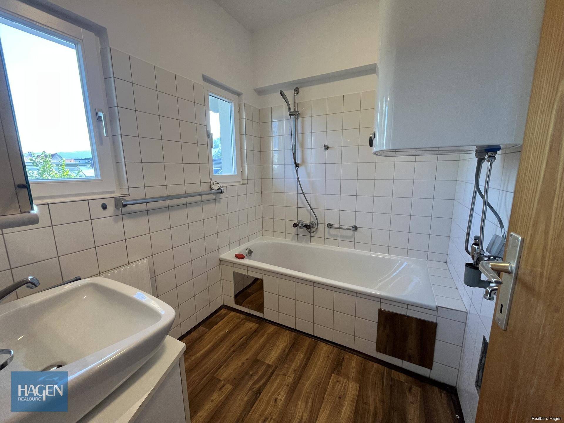 Badezimmer mit Badewanne, Dusche, Waschbecken und zwei Fenstern für gute Belüftung.