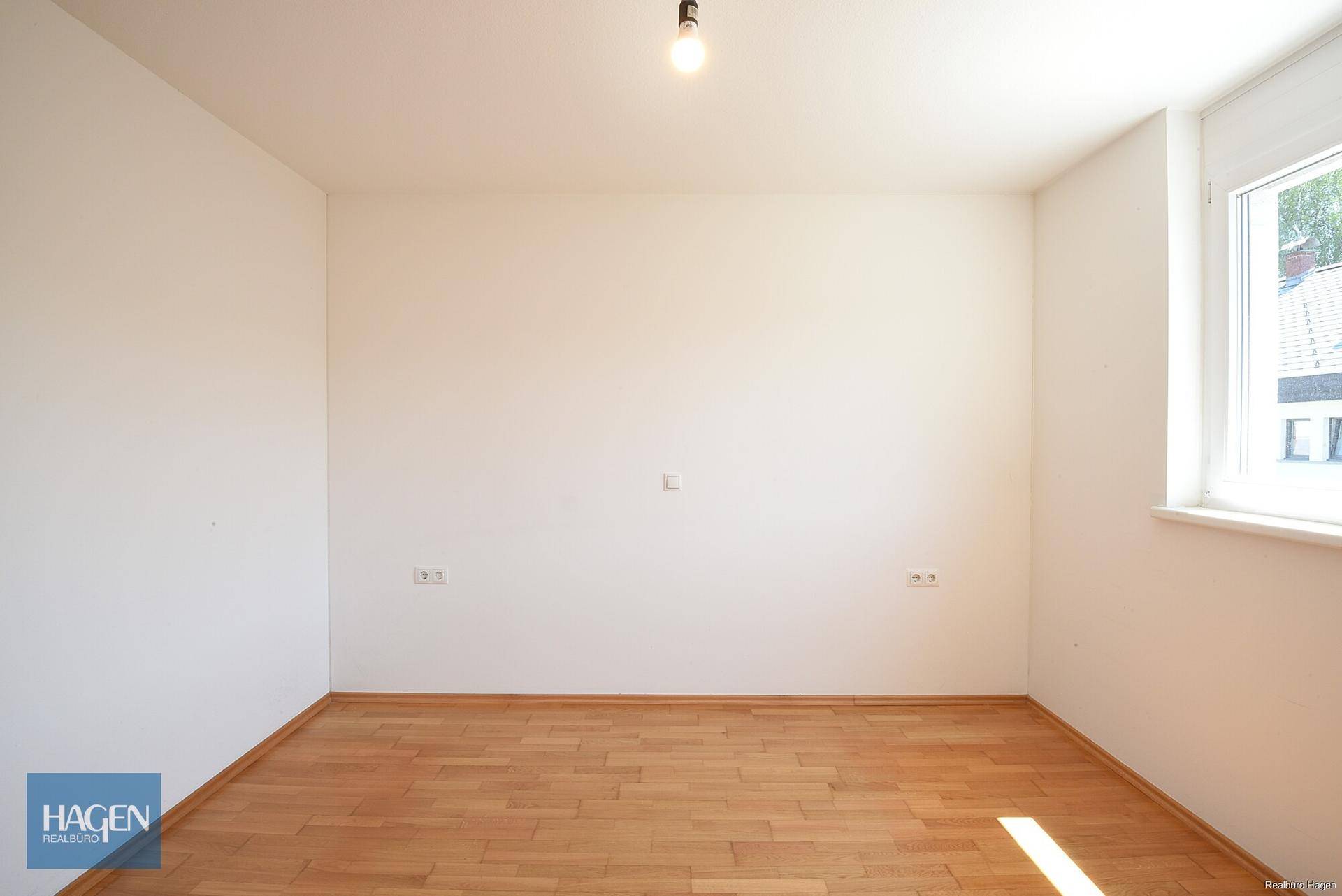 Helles Zimmer mit Holzboden und einem Fenster, das viel Tageslicht hereinlässt.