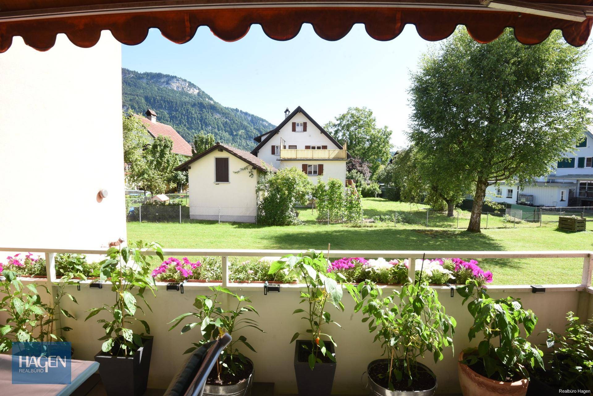 Sonniger Balkon mit Blick auf den grünen Garten und die umliegende Berglandschaft.