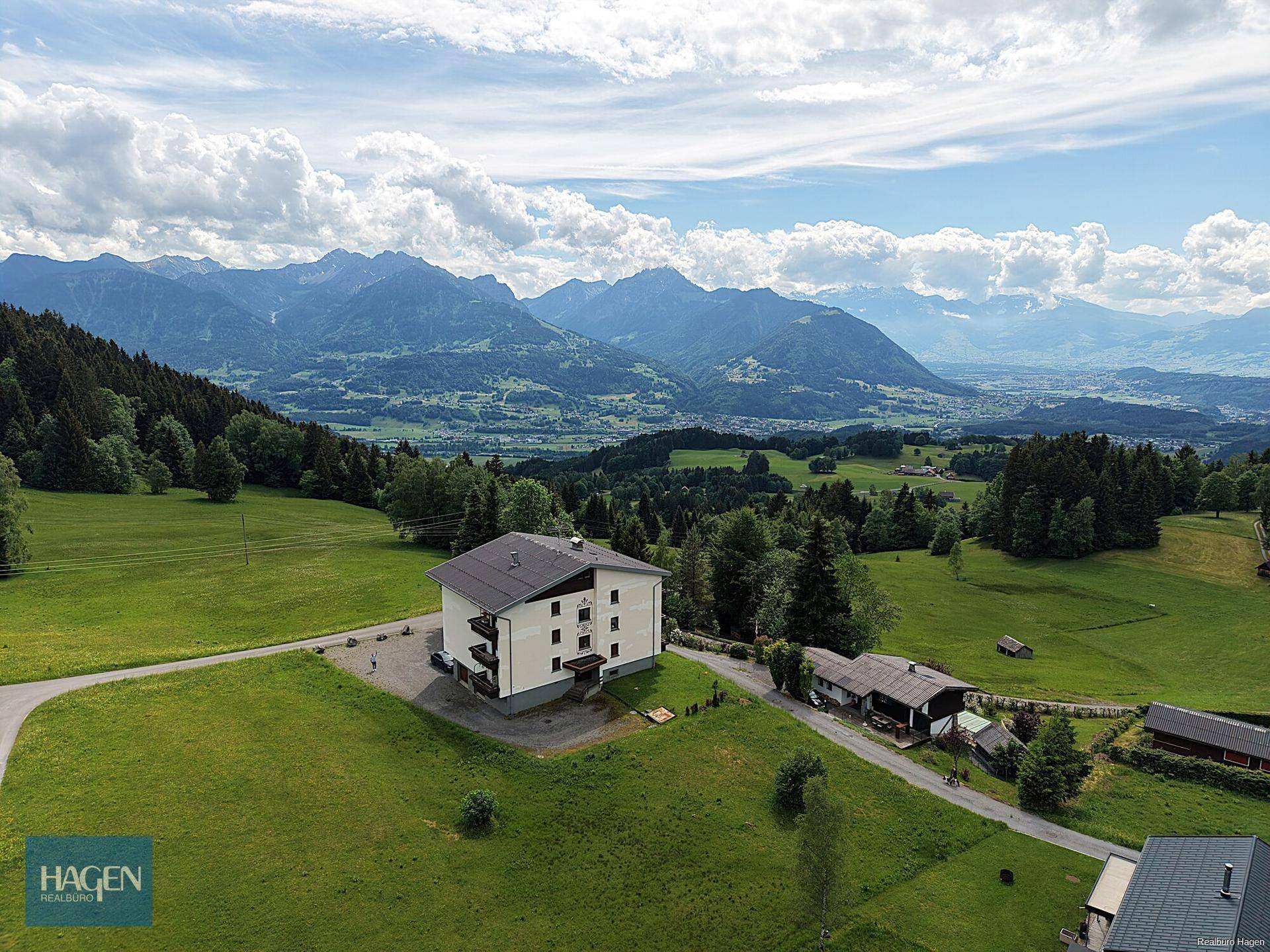 Weitläufige Luftaufnahme des Gebäudes eingebettet in die grüne Berglandschaft mit Fernblick.