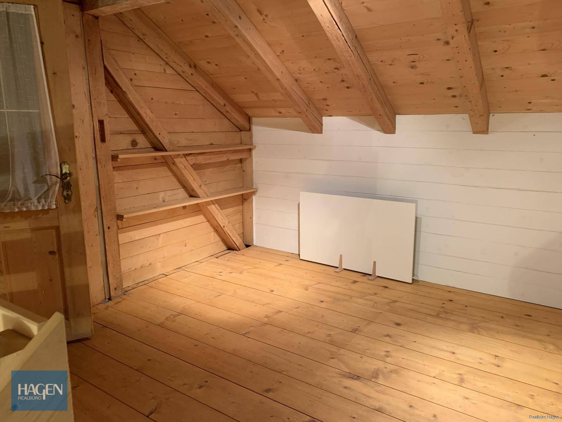 Dachgeschossraum mit sichtbaren Holzbalken, Holzdecke, Holzboden und schrägen Wänden.