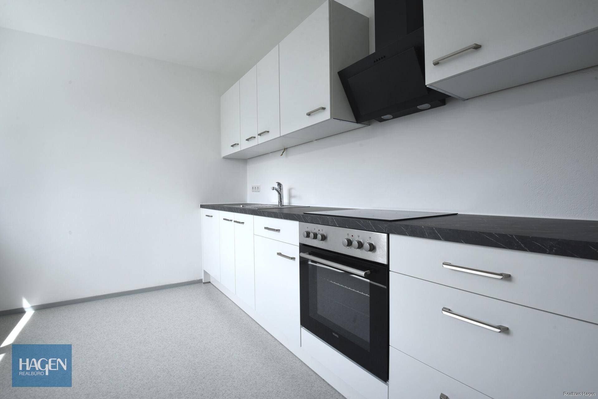 Moderne Einbauküche mit weißen Schränken, dunkler Arbeitsplatte und integrierten Geräten.
