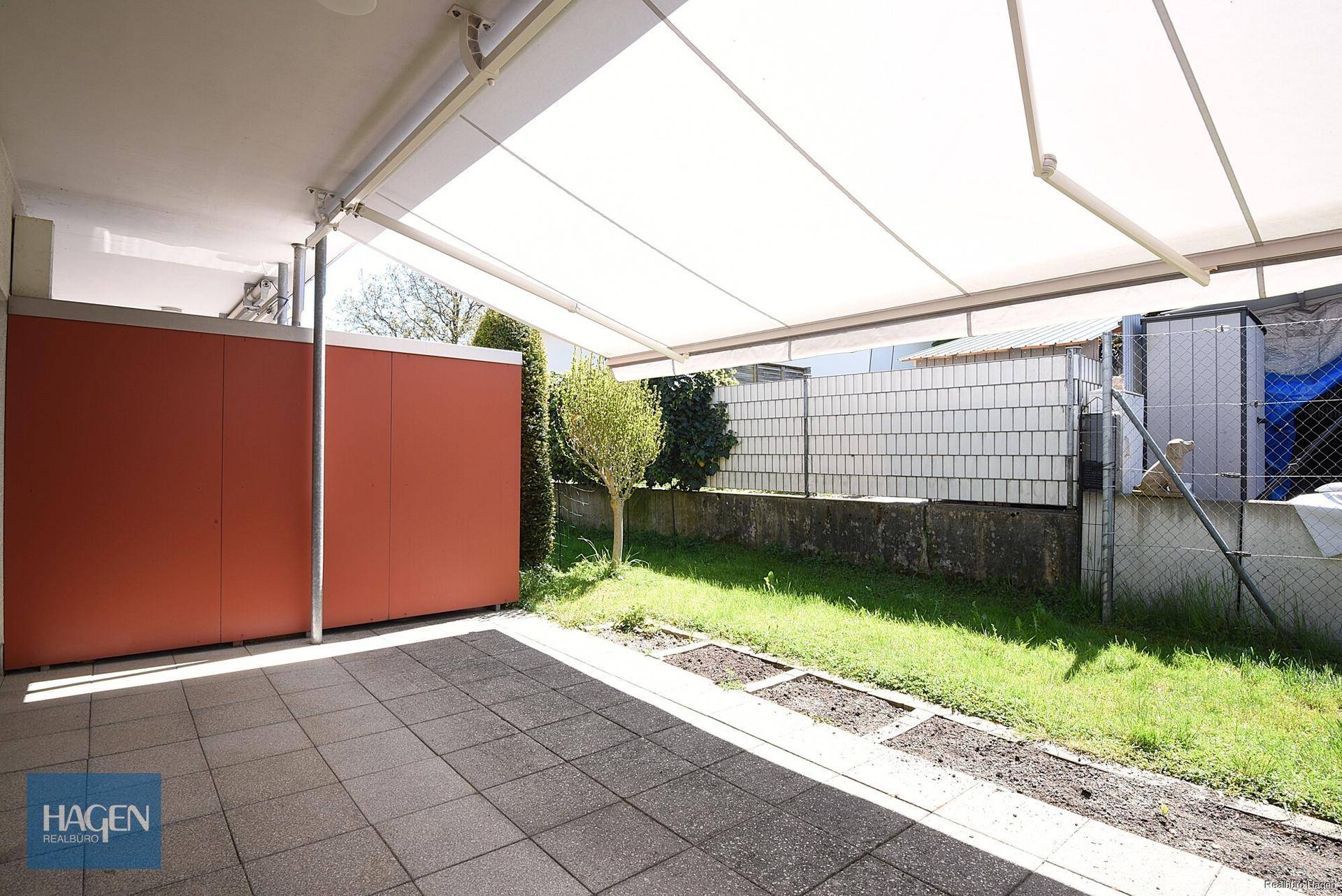 Überdachte Terrasse mit Markise, Fliesenboden und angrenzendem Gartenbereich.