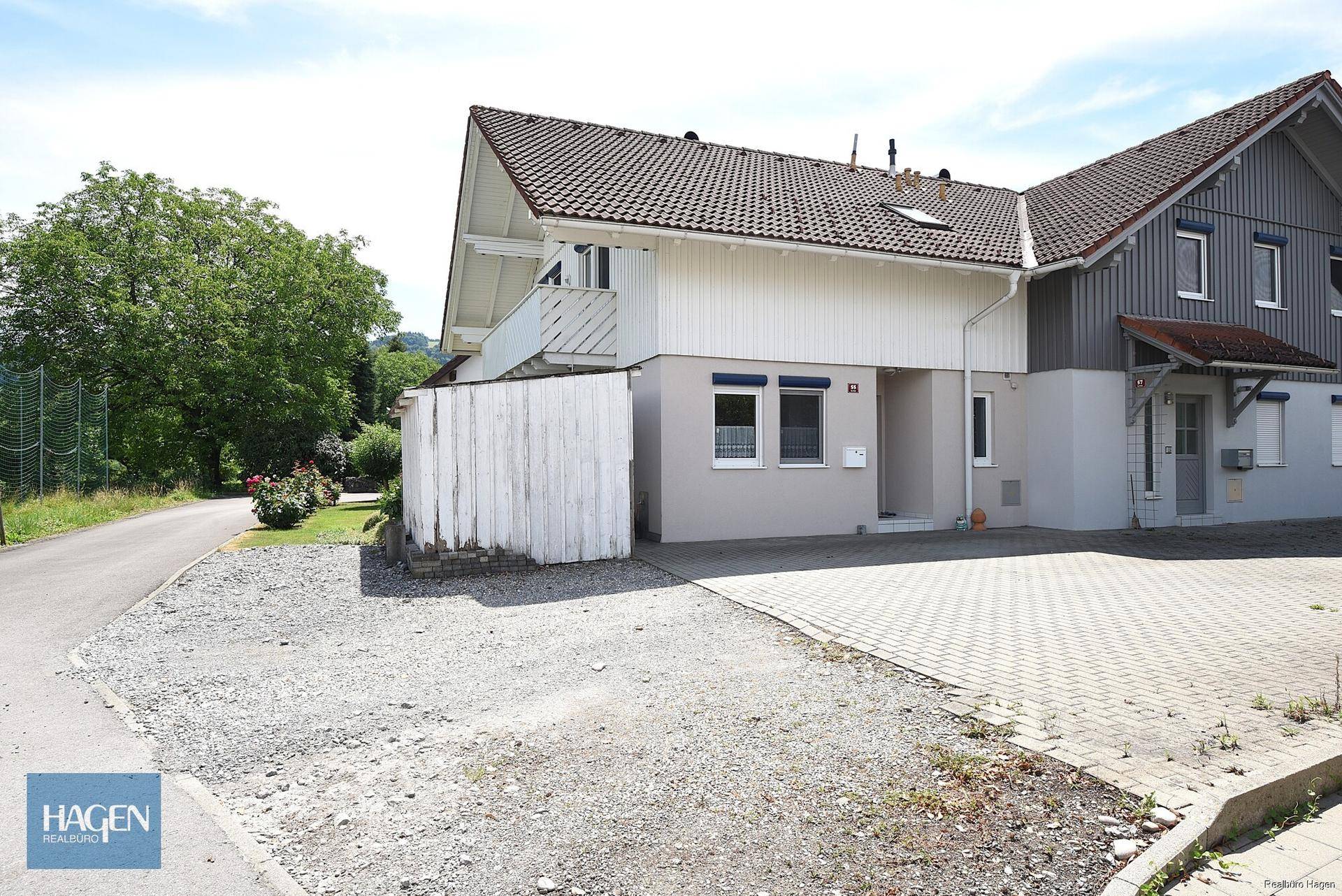 Vorderansicht des Hauses mit breiter Zufahrt, Parkmöglichkeiten und angrenzendem Grünbereich.
