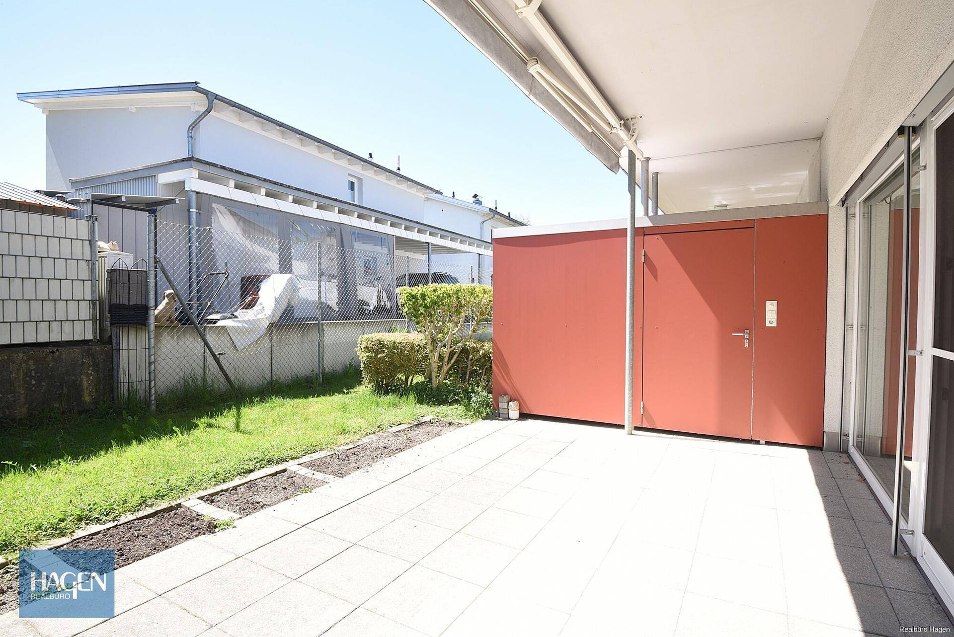Sonniger Terrassenbereich mit Fliesenboden und angrenzender kleiner Rasenfläche.