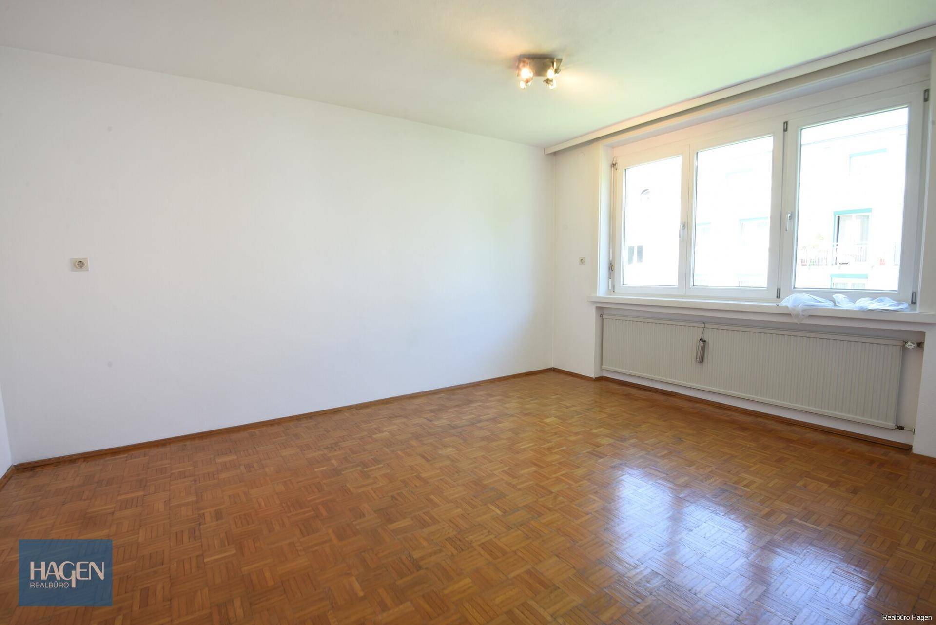 Geräumiges Wohnzimmer mit Parkettboden und großen Fenstern für viel Tageslicht.