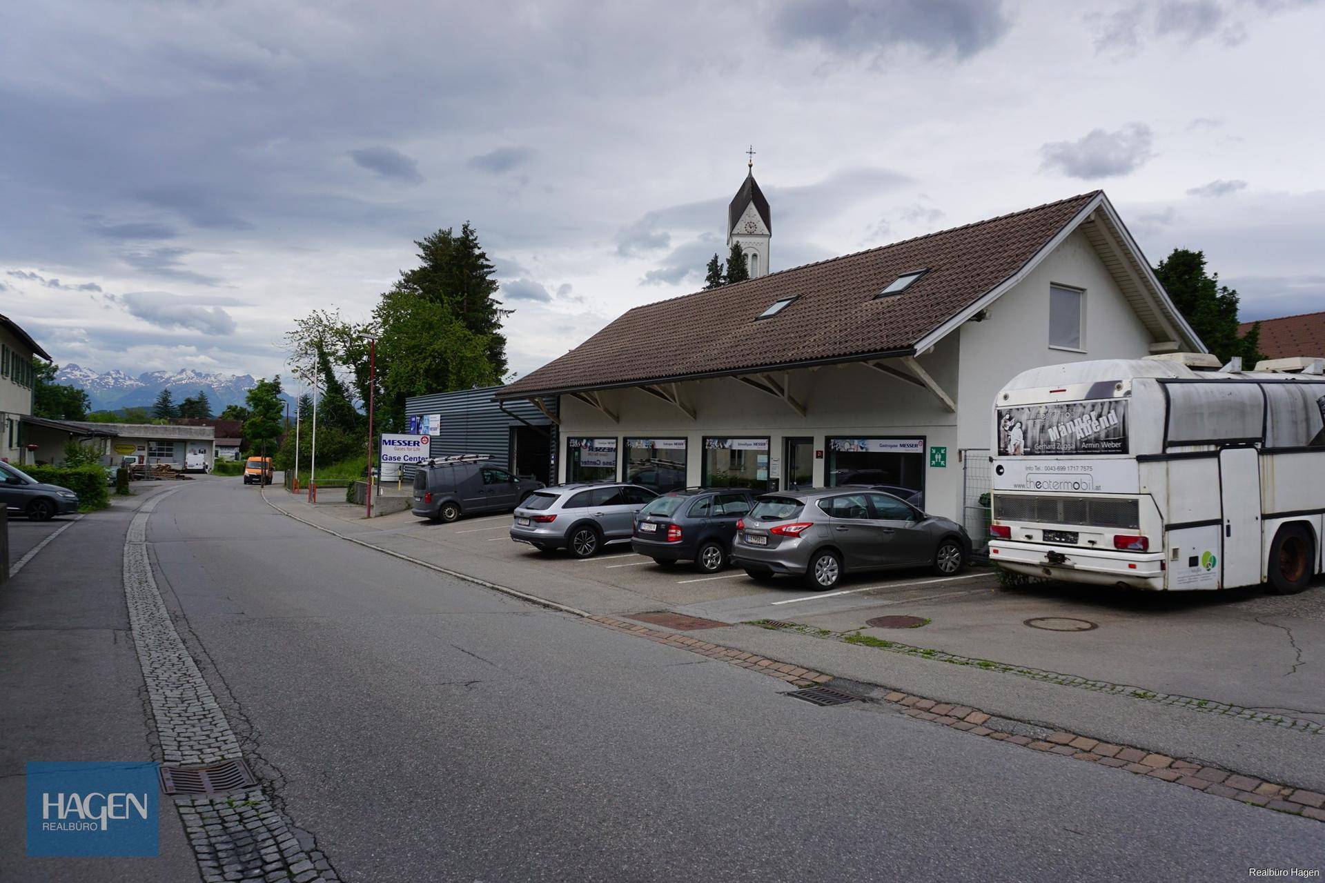Außenansicht eines Geschäftsgebäudes mit Kundenparkplätzen und einer Kirche im Hintergrund.