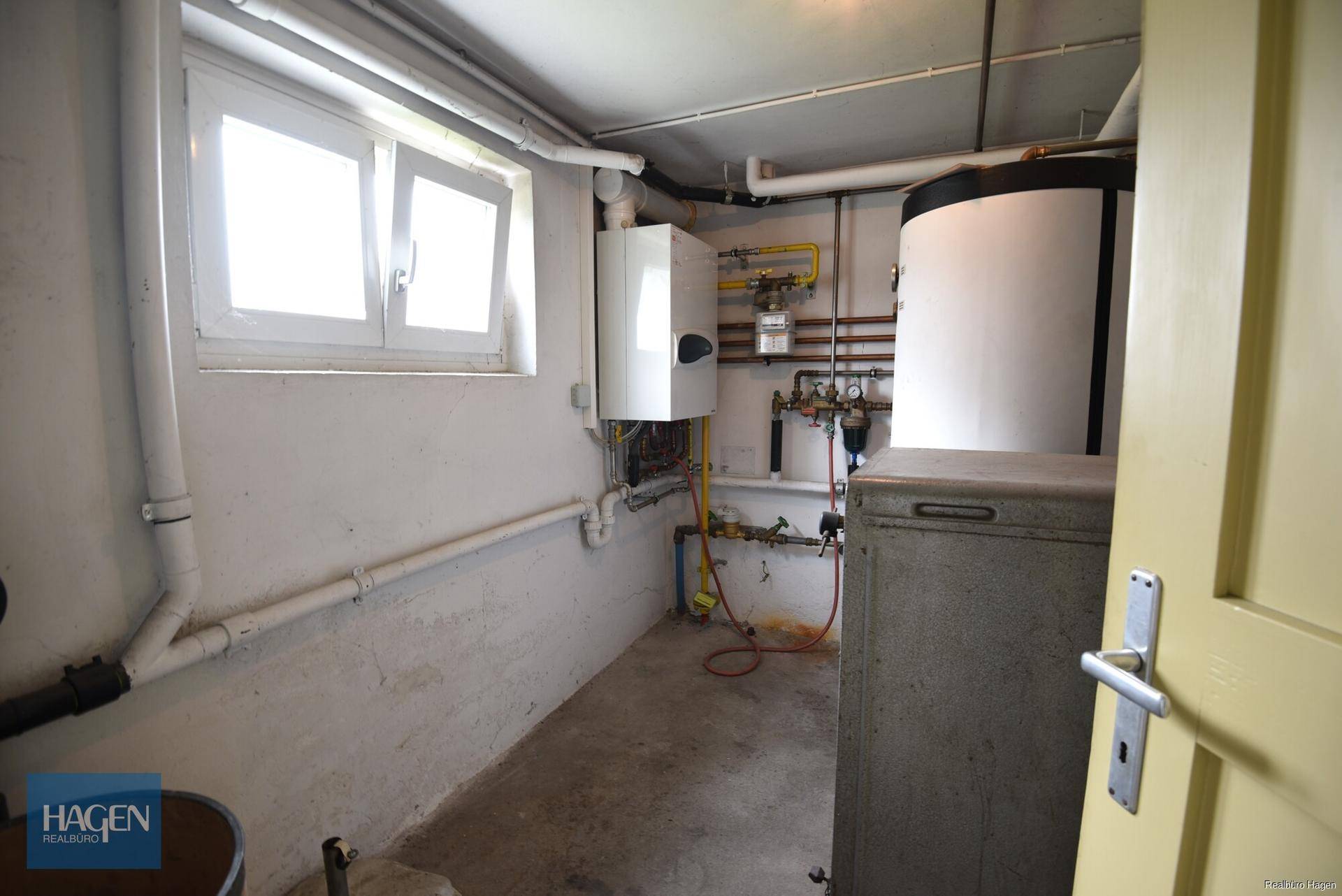 Heizungsraum im Keller mit Heizungsanlage, Warmwasserspeicher und Fenster.