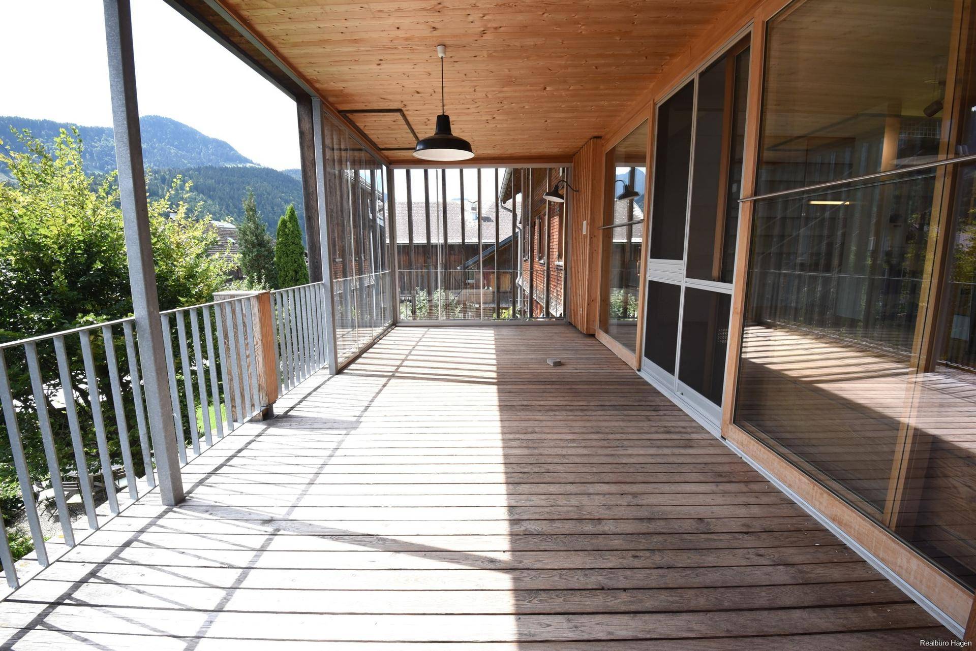Geräumige Loggia mit Holzboden und Metallgeländer, bietet einen geschützten Außenbereich mit Bergblick.