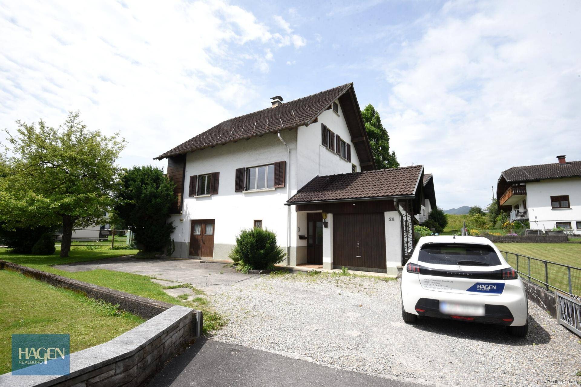 Einfamilienhaus mit weißer Fassade, braunen Fensterläden und gepflasterter Zufahrt.