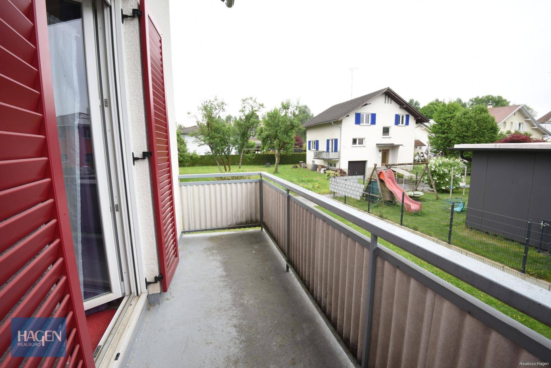 Balkon mit Metallgeländer und Blick auf den Garten und die Nachbarschaft.