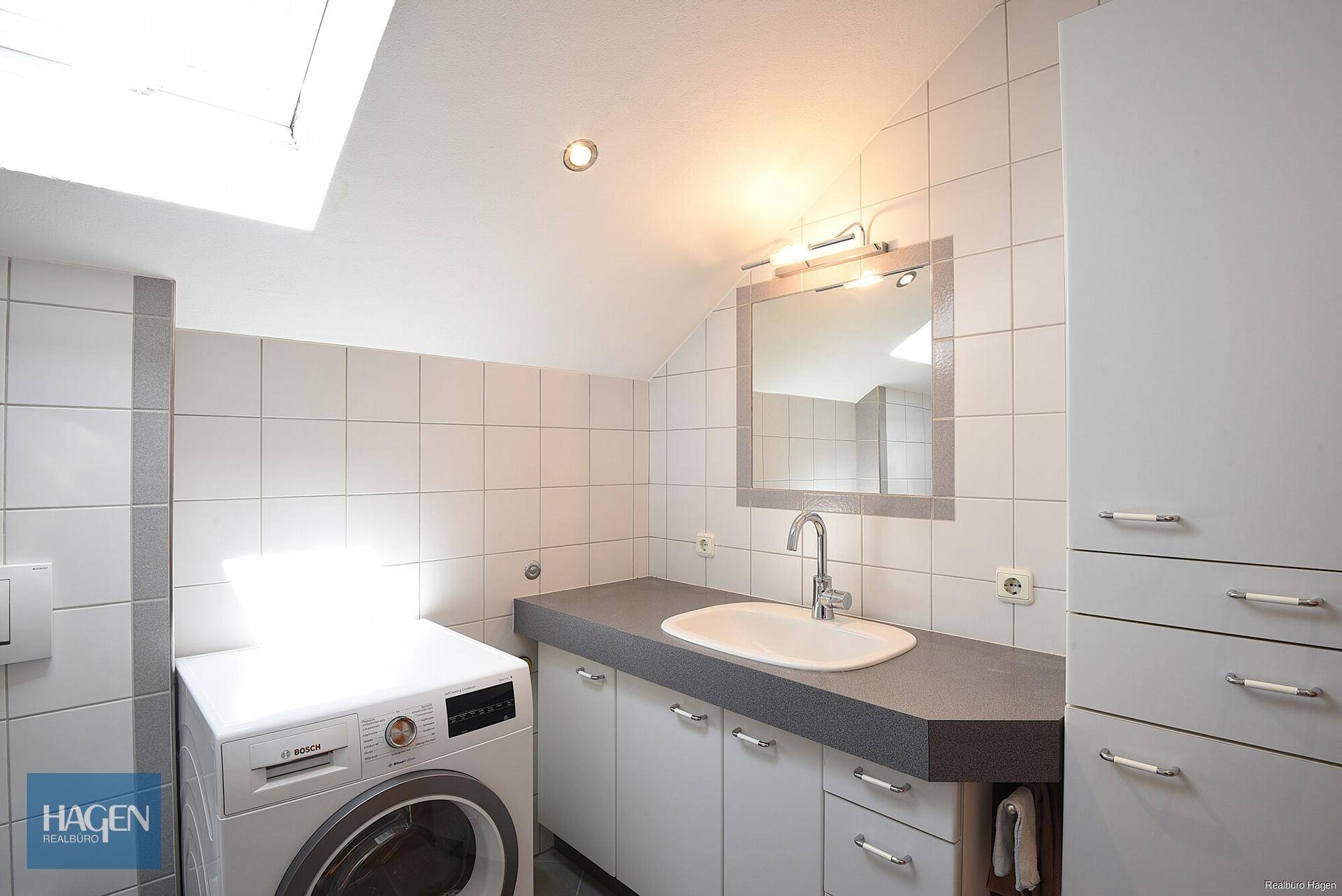 Modernes Badezimmer mit Waschmaschine, Waschbecken, Spiegelschrank und Dachfenster.