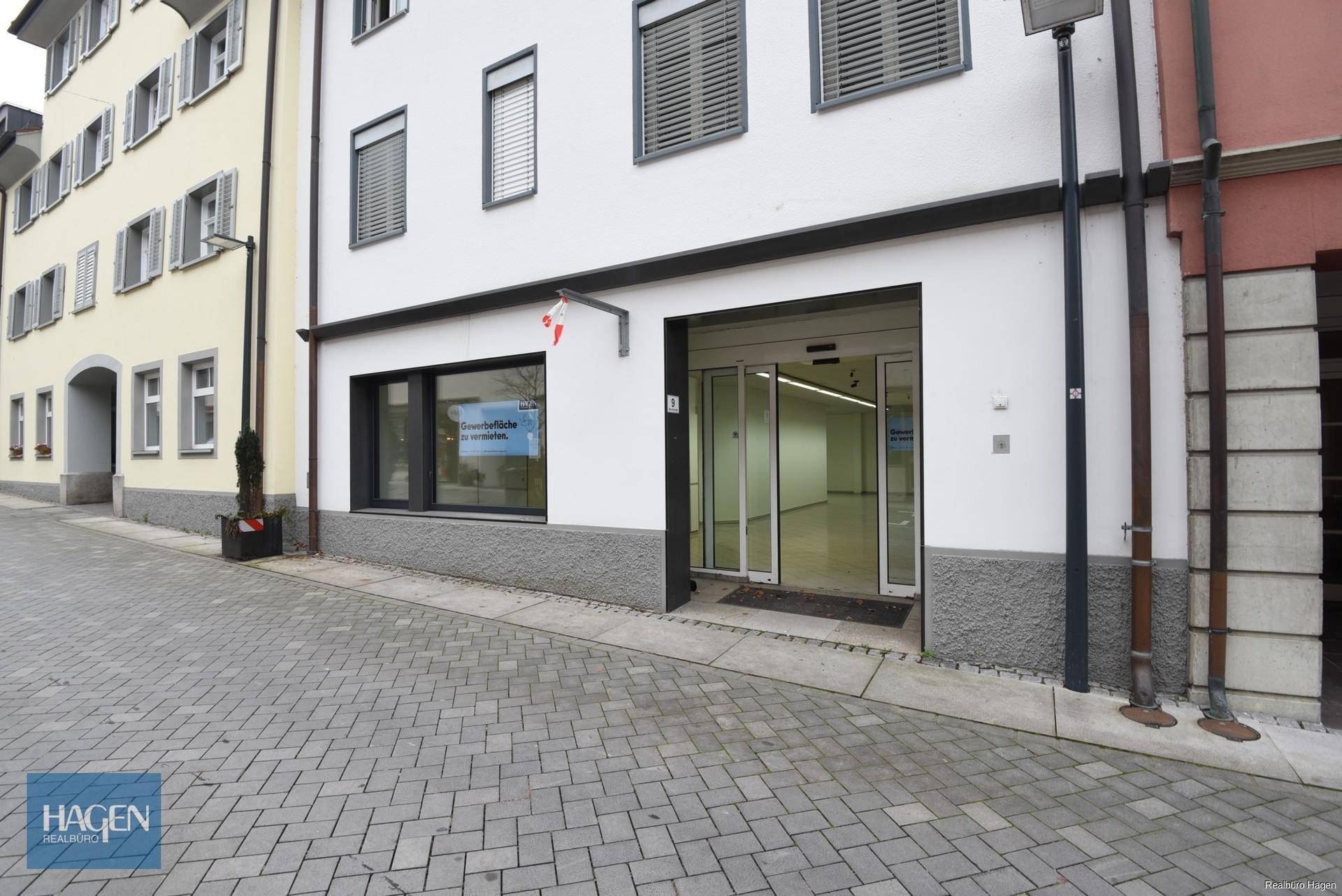 Eingangsbereich des Geschäfts mit automatischen Glastüren und Schaufenstern zur Straße hin.