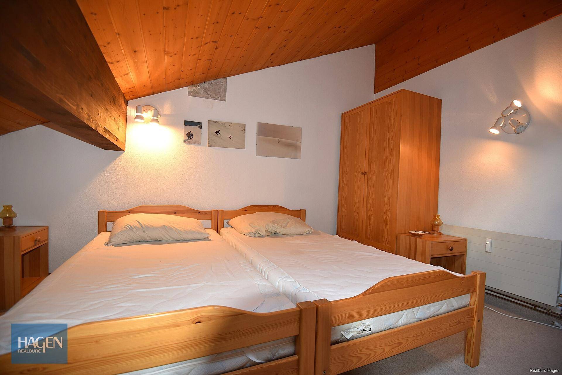 Schlafzimmer mit zwei Einzelbetten, Holzmöbeln und einer gemütlichen Dachschräge mit Holzverkleidung.