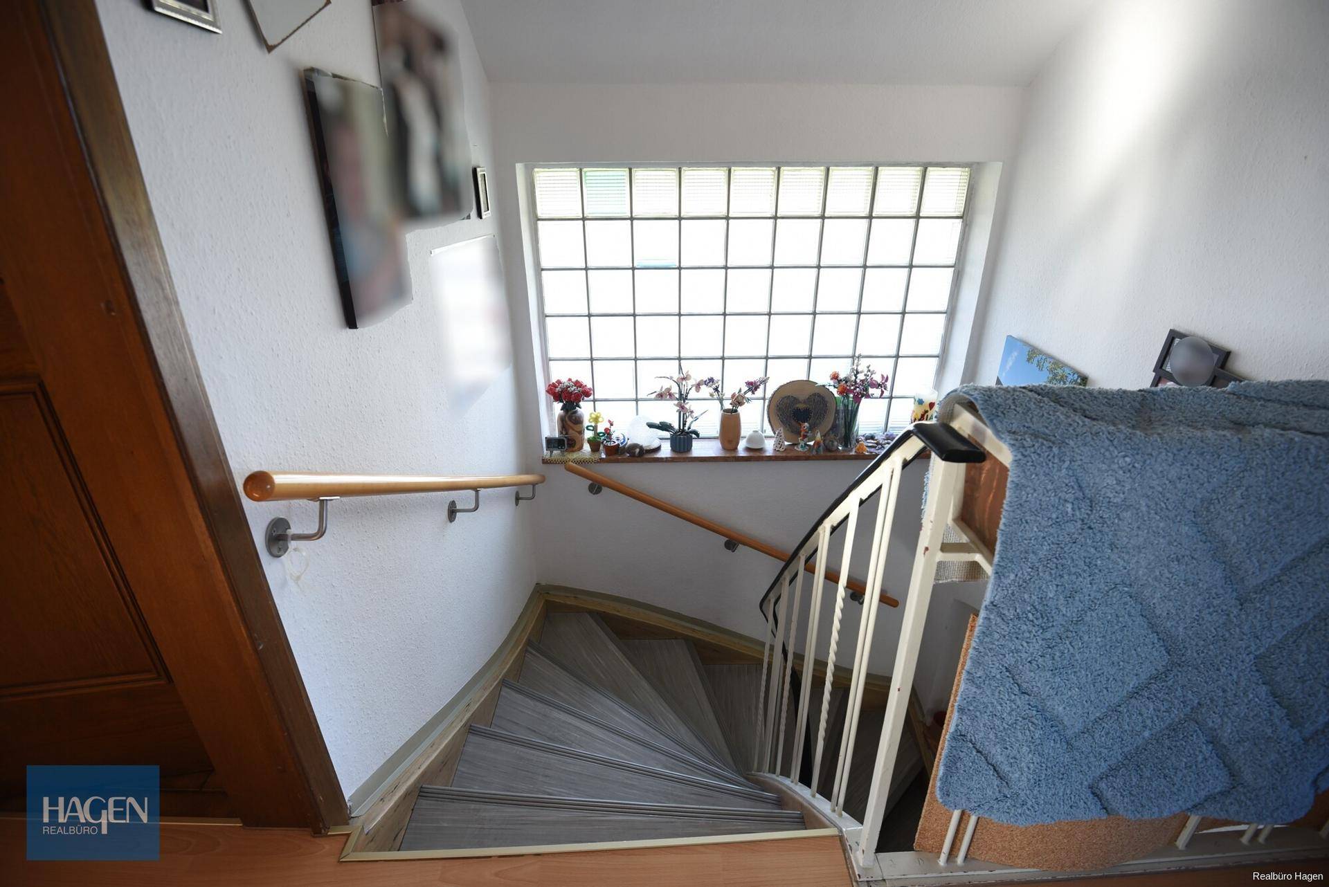 Treppenhaus mit Holzgeländer und einem großen Glasbausteinfenster für viel Licht.