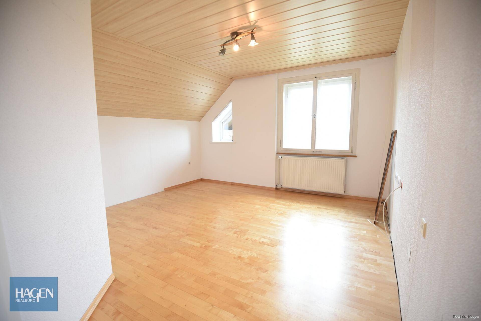 Helles Dachgeschosszimmer mit Holzboden, schrägen Wänden und zwei Fenstern.