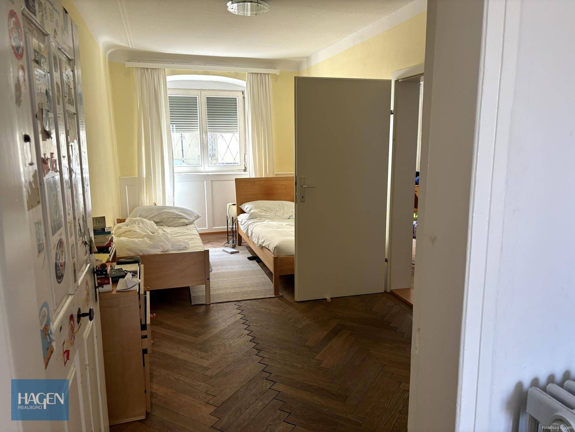 Schlafzimmer mit zwei Betten, Parkettboden und Fenster mit Blick ins Grüne.