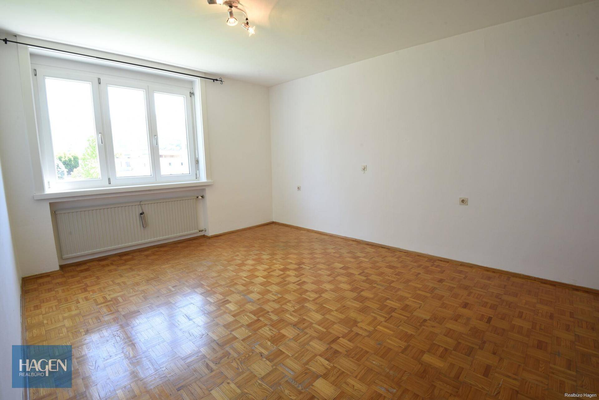 Heller Wohnraum mit klassischem Parkettboden und Ausblick ins Grüne.
