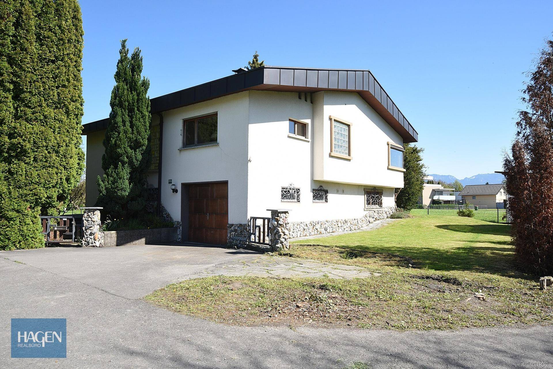 Einfamilienhaus mit integrierter Garage, gepflegtem Vorgarten und breiter Auffahrt unter blauem Himmel.