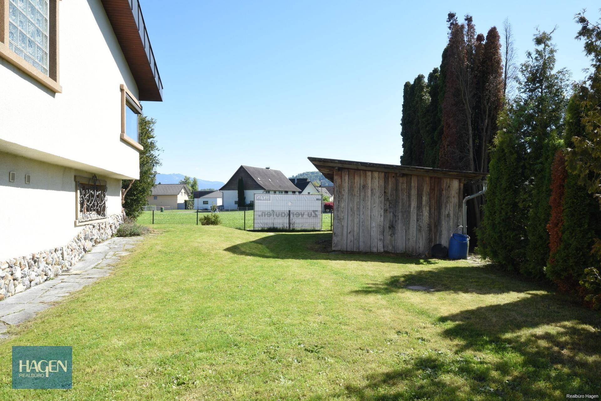 Gepflegter Gartenbereich mit Rasenfläche, Gartenhaus und Blick auf die umliegende Landschaft.