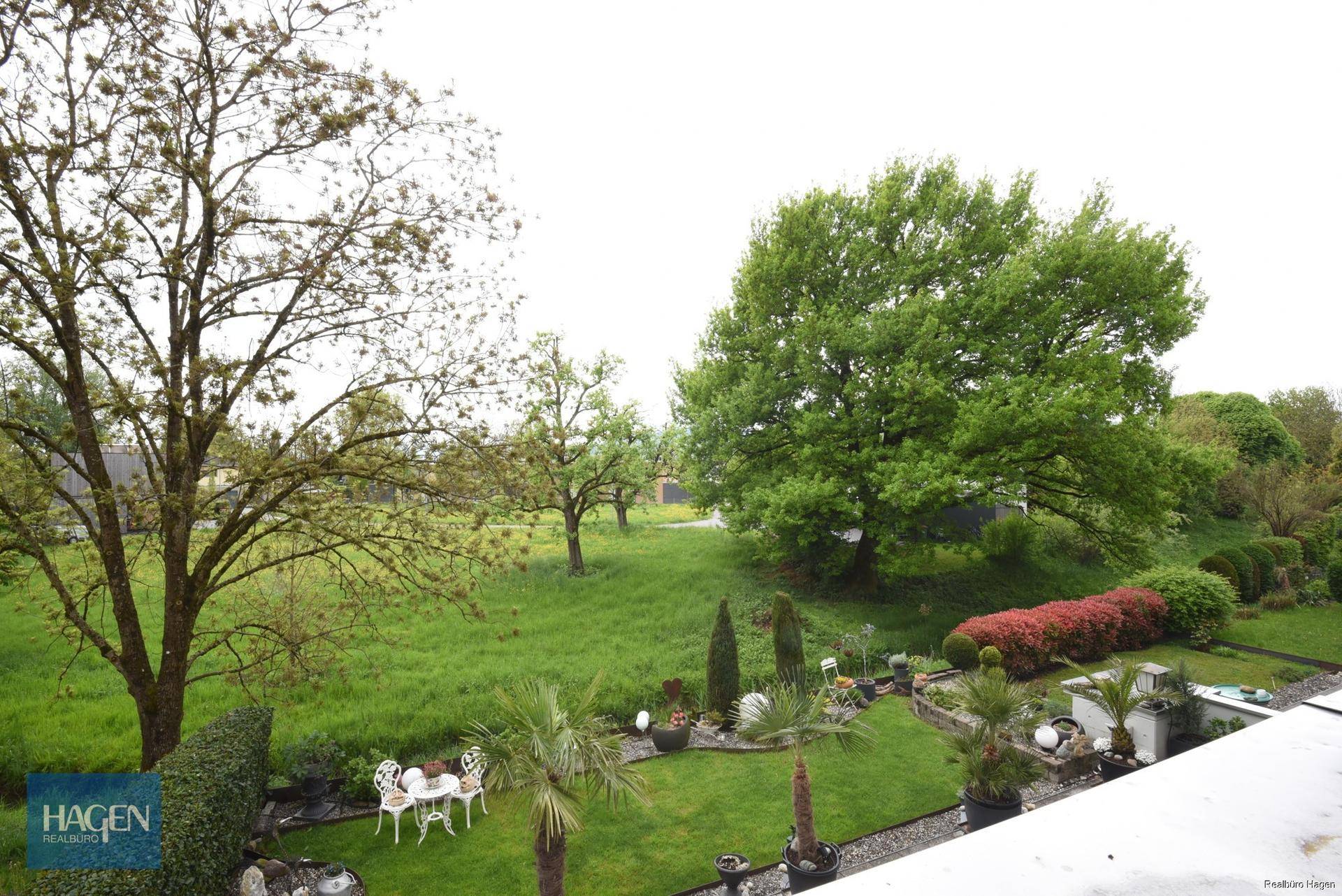Malerischer Gartenbereich mit üppigem Grün, Bäumen und einer kleinen Sitzgelegenheit.