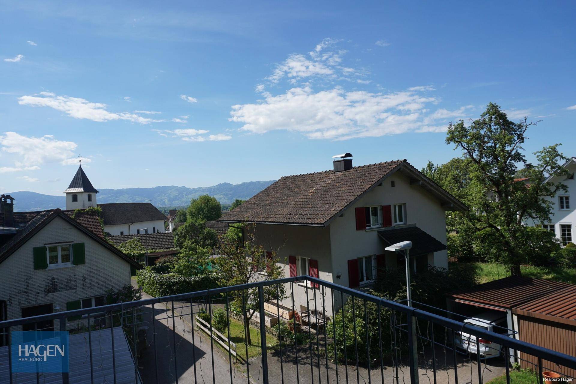 Ausblick von einem Balkon auf die Nachbarschaft mit Kirchturm und die malerische Bergkulisse.