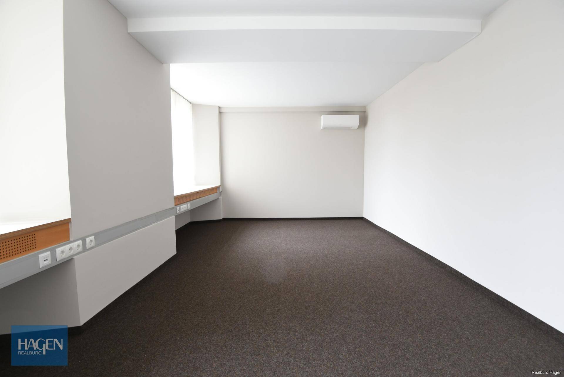 Helles, leeres Büro mit weiß gestrichenen Wänden, braunem Teppichboden und Klimaanlage.