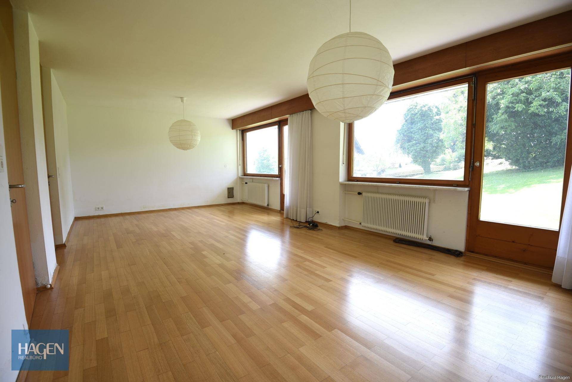 Geräumiger Raum mit Holzboden, großen Fenstern und Zugang zum Garten.