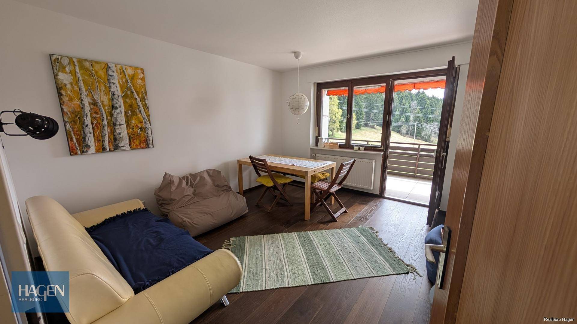 Heller Wohn- und Essbereich mit Holzboden, Zugang zum Balkon und Blick ins Grüne.