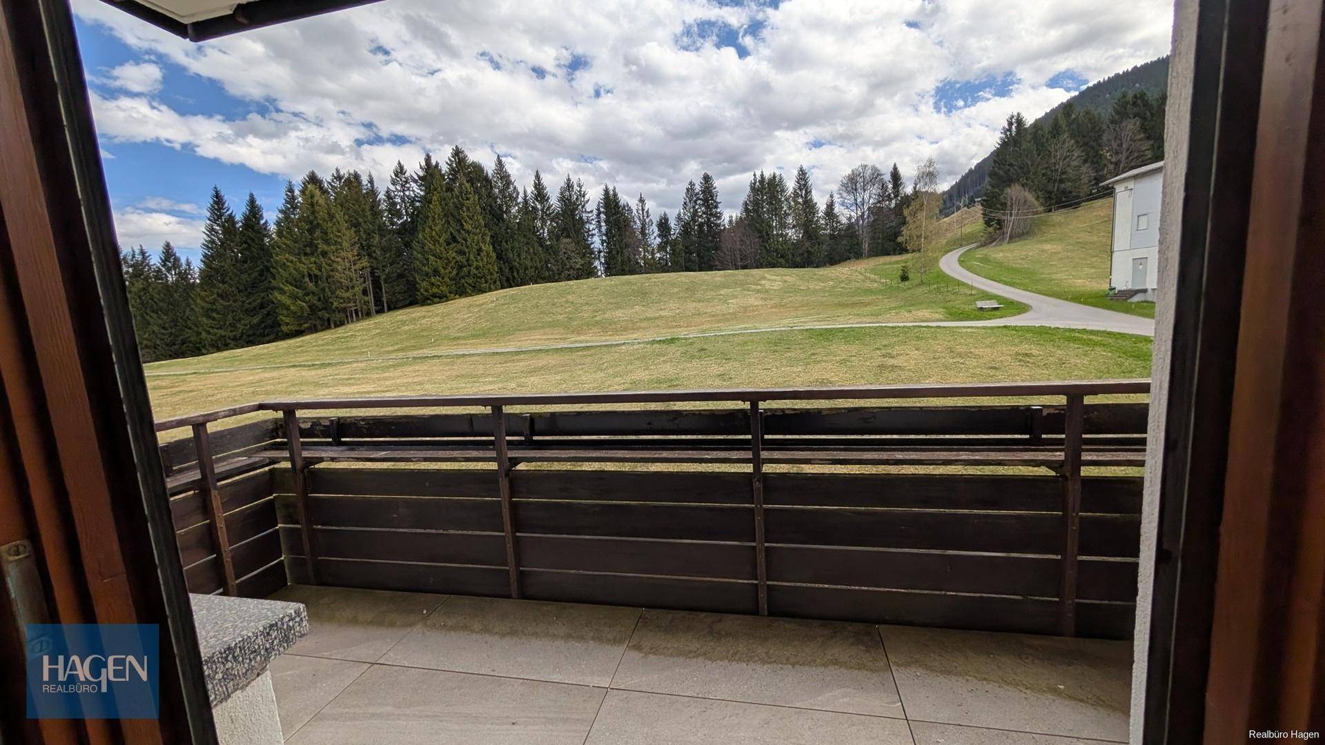 Balkon mit Fliesenboden und Holzgeländer, bietet einen weiten Blick auf die grüne Hügellandschaft.