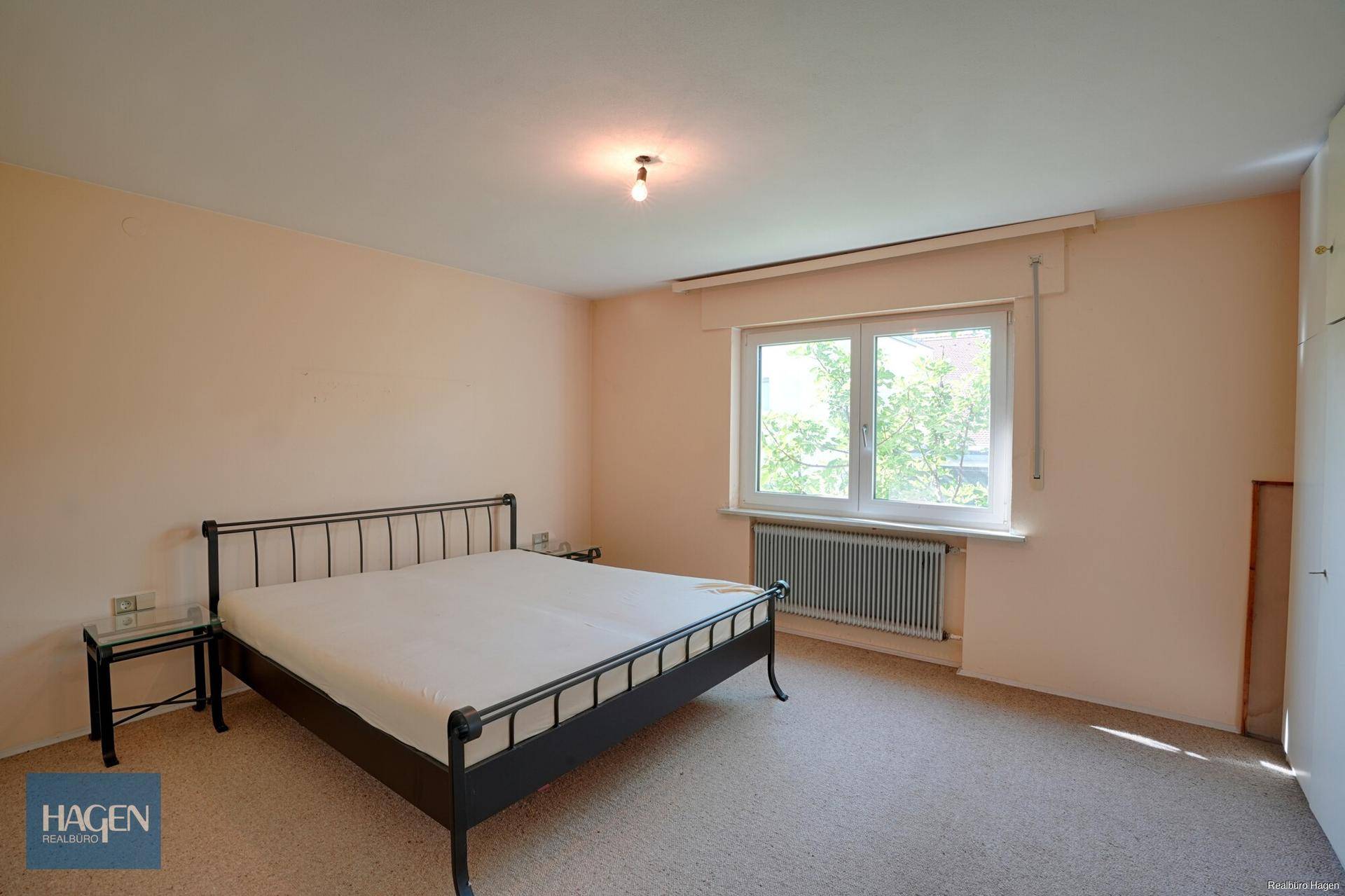 Helles Schlafzimmer mit Doppelbett, Teppichboden und großem Fenster.