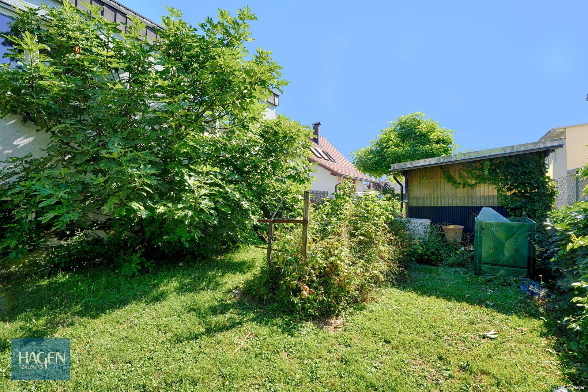 Grüner Gartenbereich mit Rasen, Bäumen und einem kleinen Schuppen.