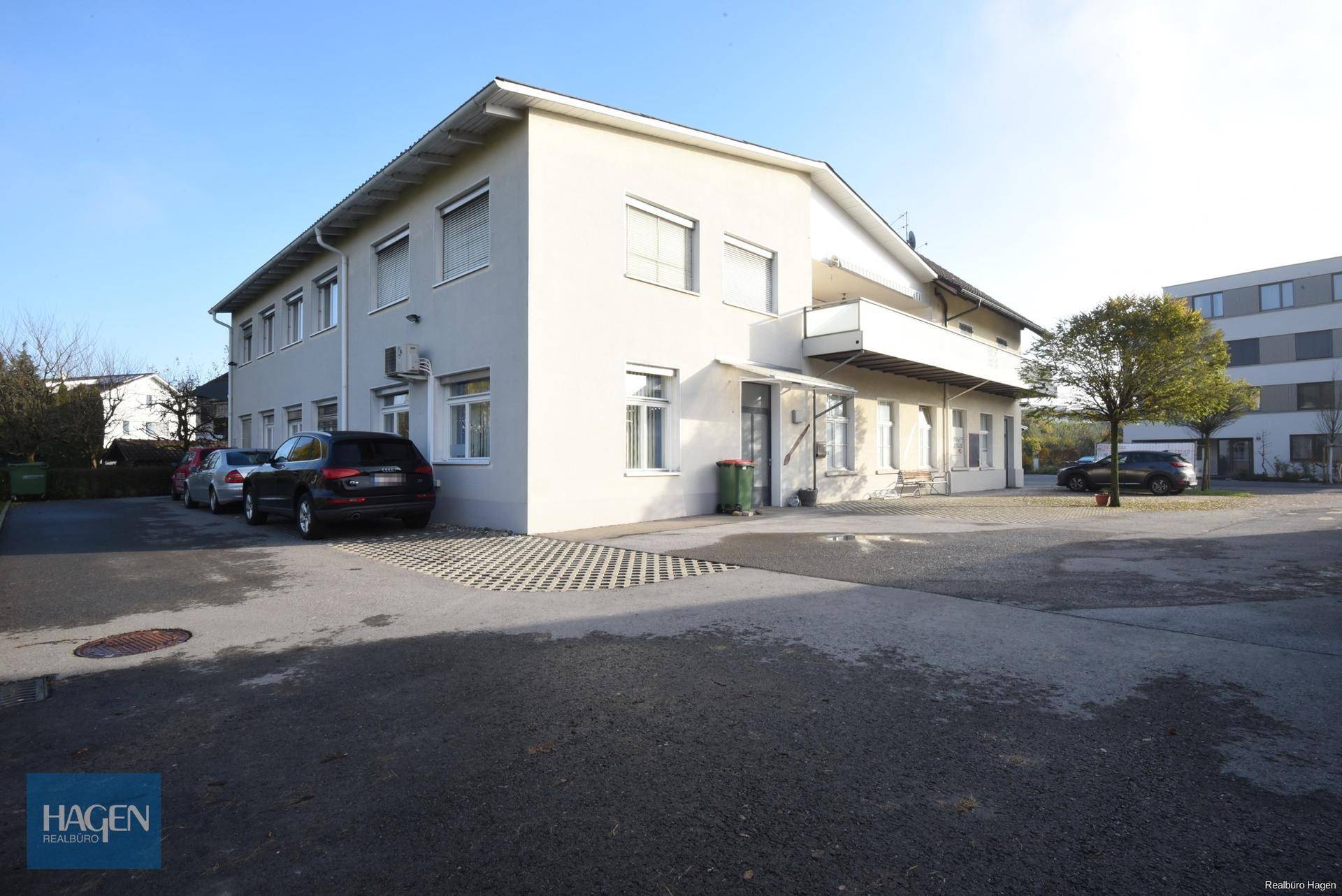 Seitenansicht des Gebäudes mit mehreren Fenstern, einem Balkon und Parkplätzen im Freien.
