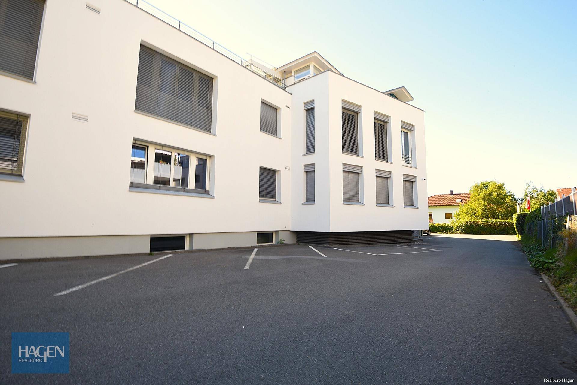 Seitenansicht des modernen weißen Gebäudes mit Parkplätzen und großen Fenstern.