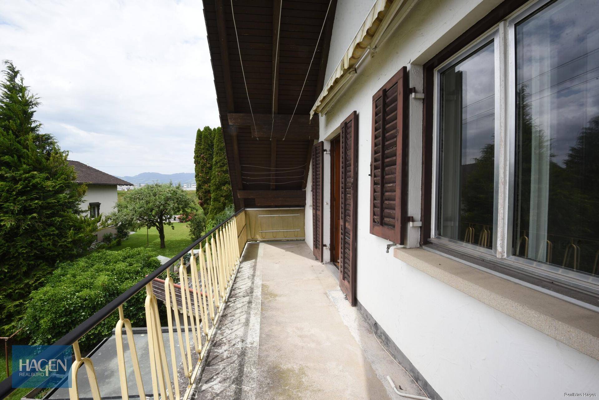 Langer Balkon mit Metallgeländer und Blick auf den Garten und die Umgebung.