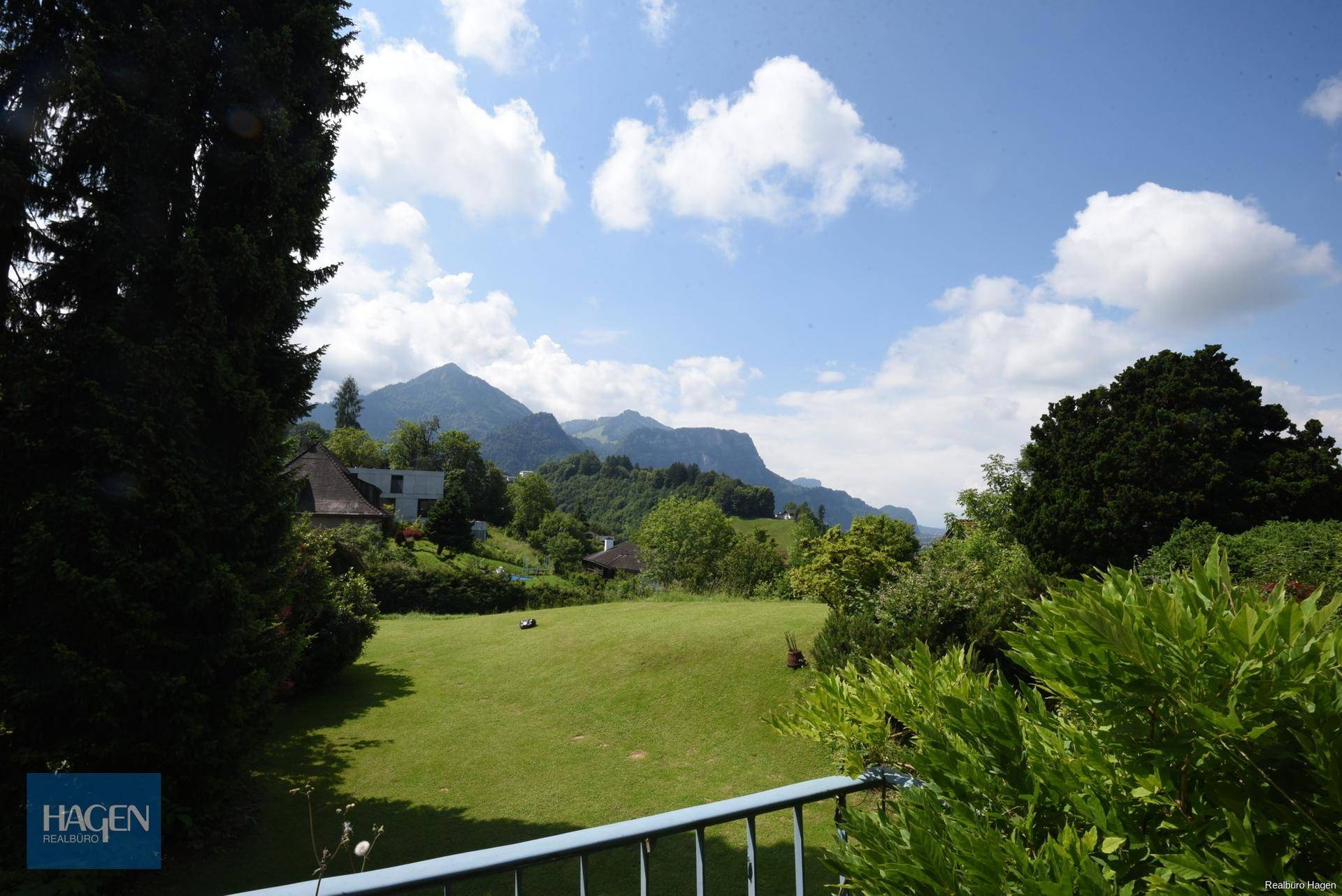 Weitläufiger Blick vom Balkon über den grünen Garten und die majestätische Berglandschaft.