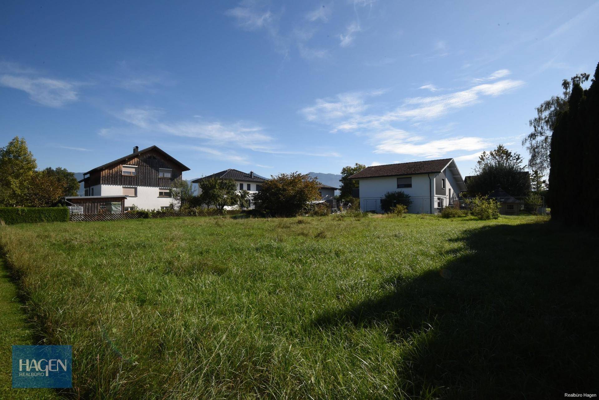Sonniges Grundstück mit Bergblick und angrenzenden Wohnhäusern in ländlicher Umgebung.
