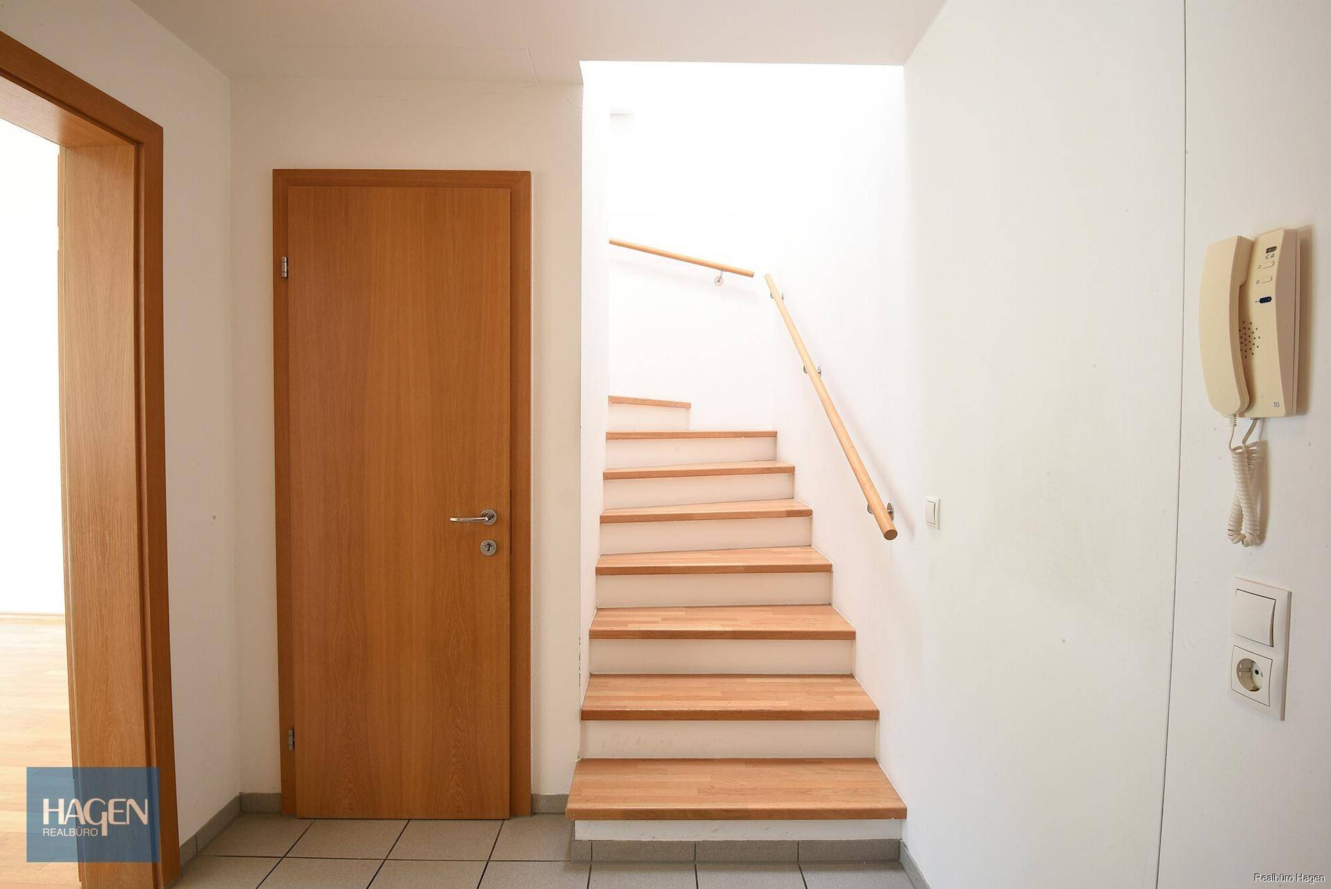 Eingangsbereich mit Holztreppe, Fliesenboden und einer Holztür, die zu den Wohnräumen führt.
