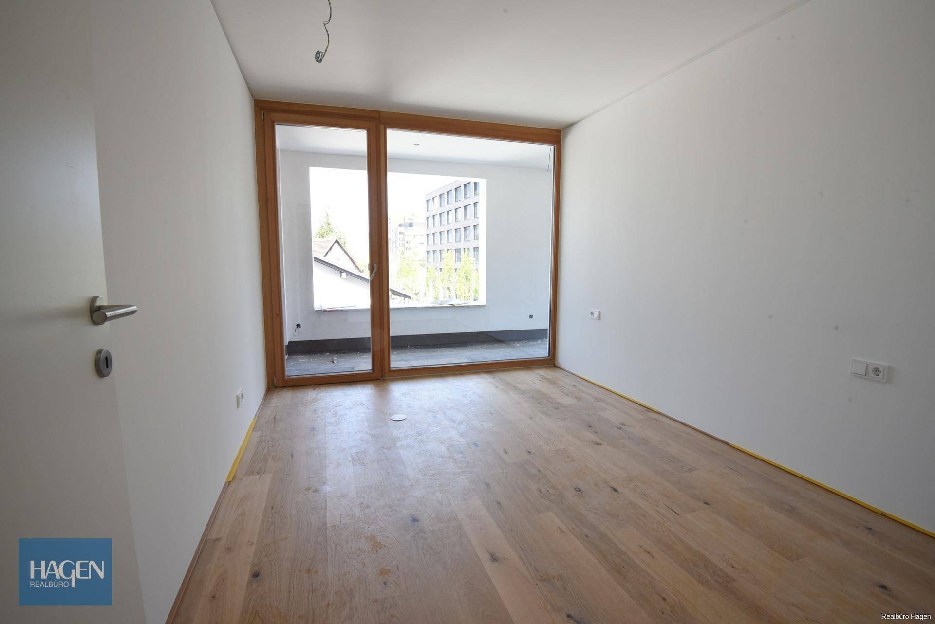 Helles, leeres Zimmer mit Holzboden und breiter Schiebetür zum Außenbereich.
