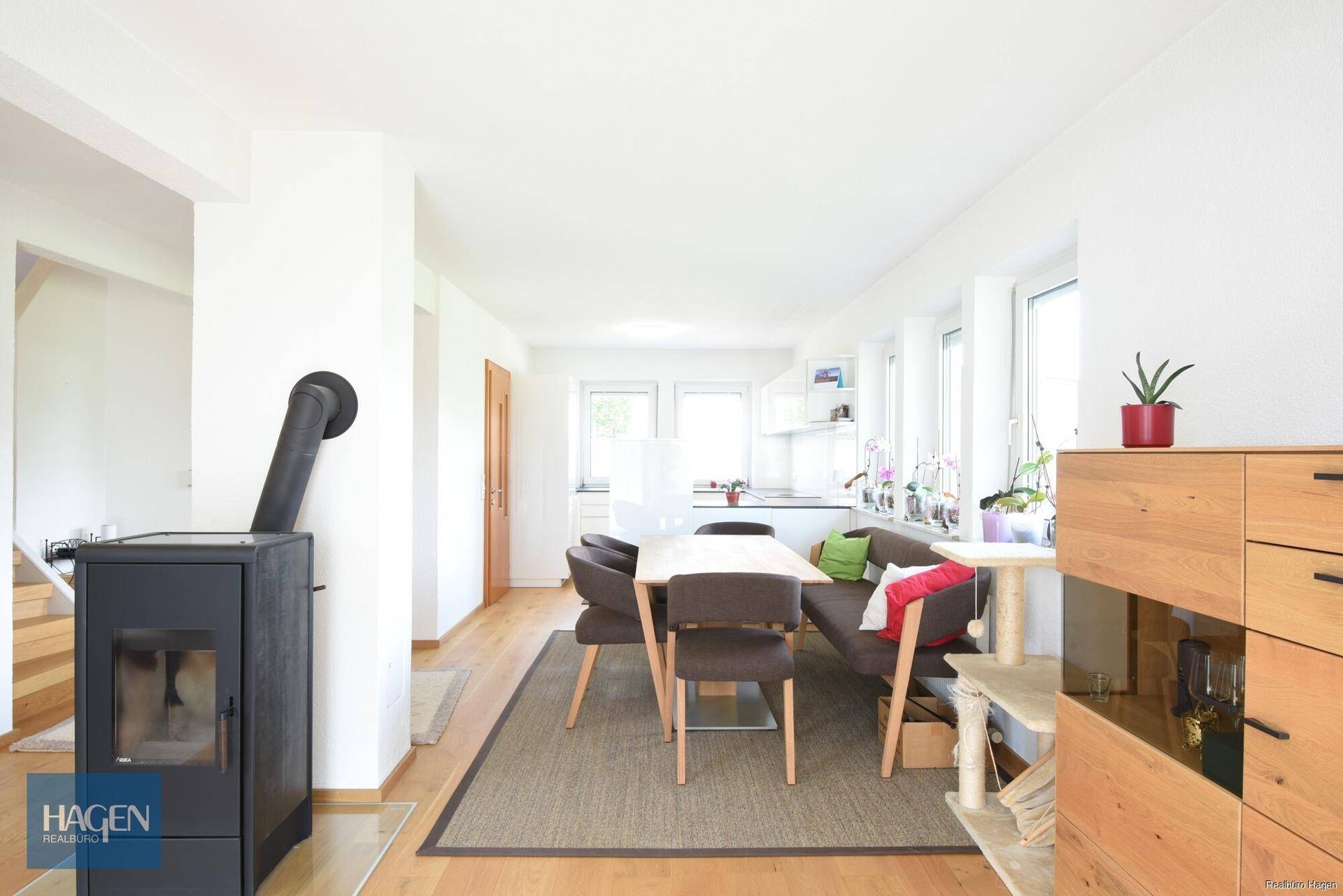 Heller offener Wohn-Essbereich mit Holzboden, modernem Kaminofen und viel Tageslicht.