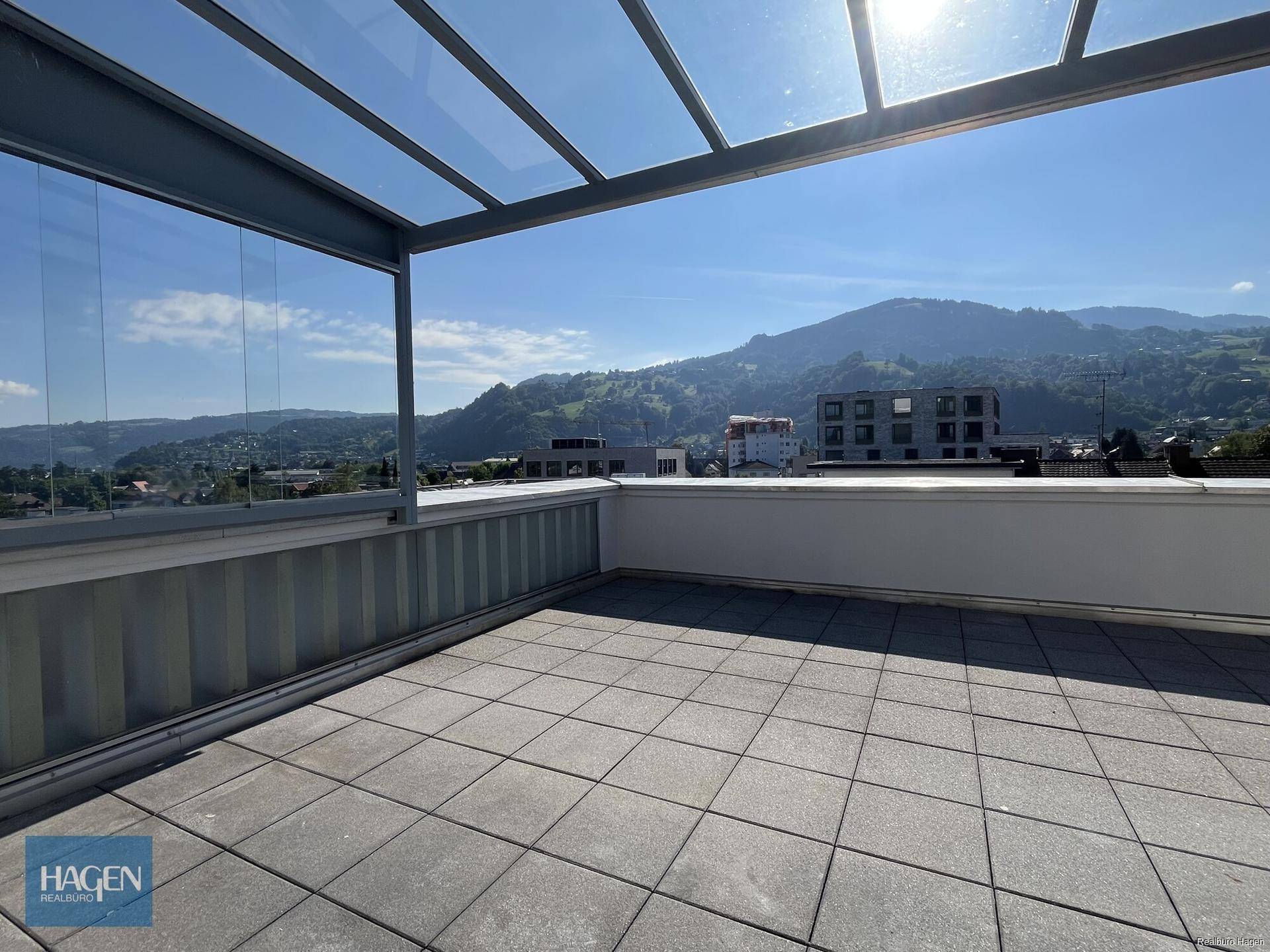 Weitläufige Dachterrasse mit Glasüberdachung und Panoramablick auf die Stadt und Berge.