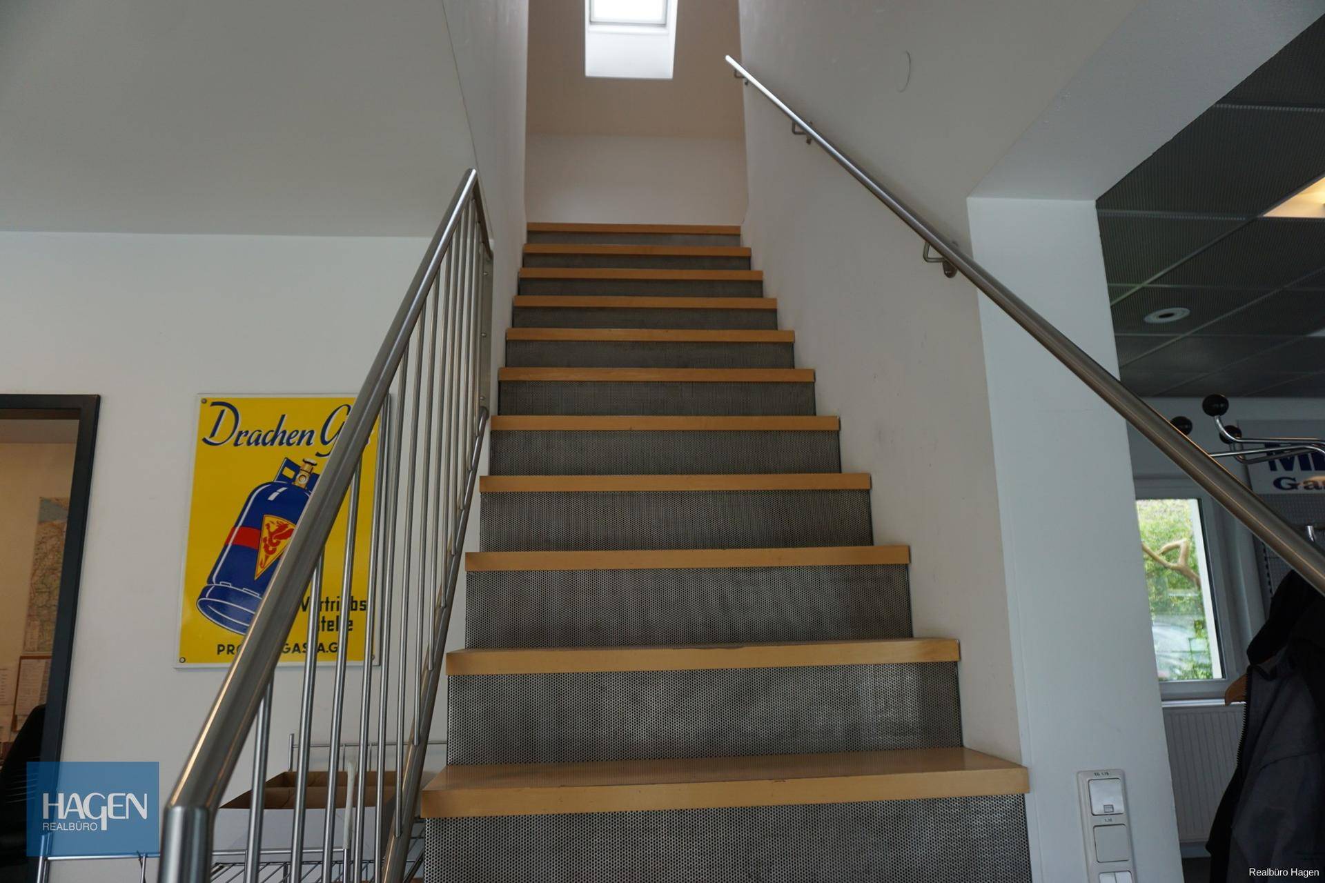 Moderne Treppe mit Holzstufen und Edelstahlgeländer, die in ein Obergeschoss führt.
