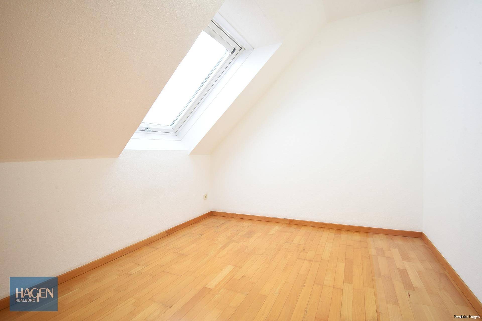 Leerer Dachbodenraum mit schrägem Dachfenster und hellem Laminatboden.