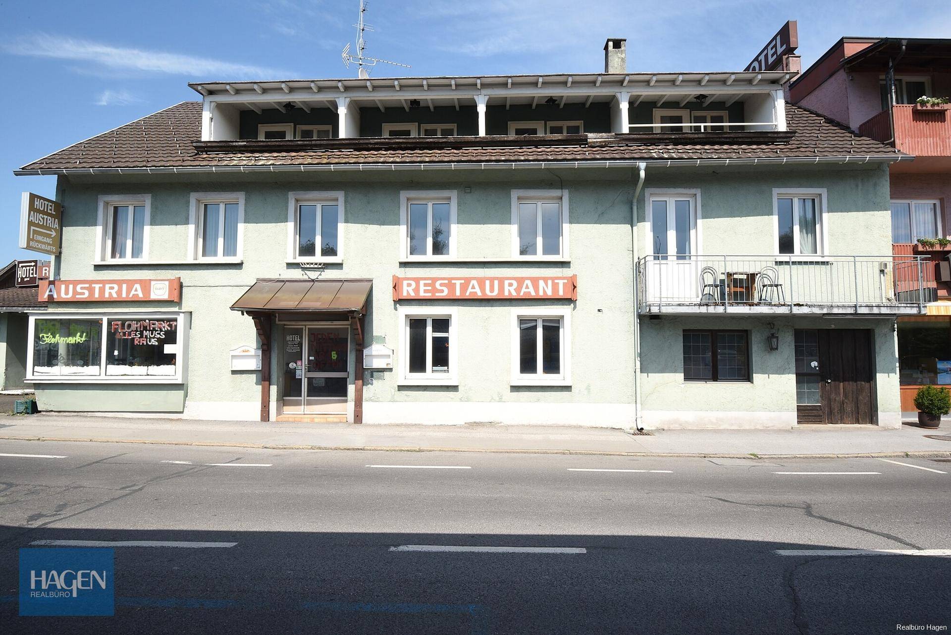 Vorderansicht eines Gebäudes mit Restaurant- und Hotelschildern sowie einem kleinen Balkon.
