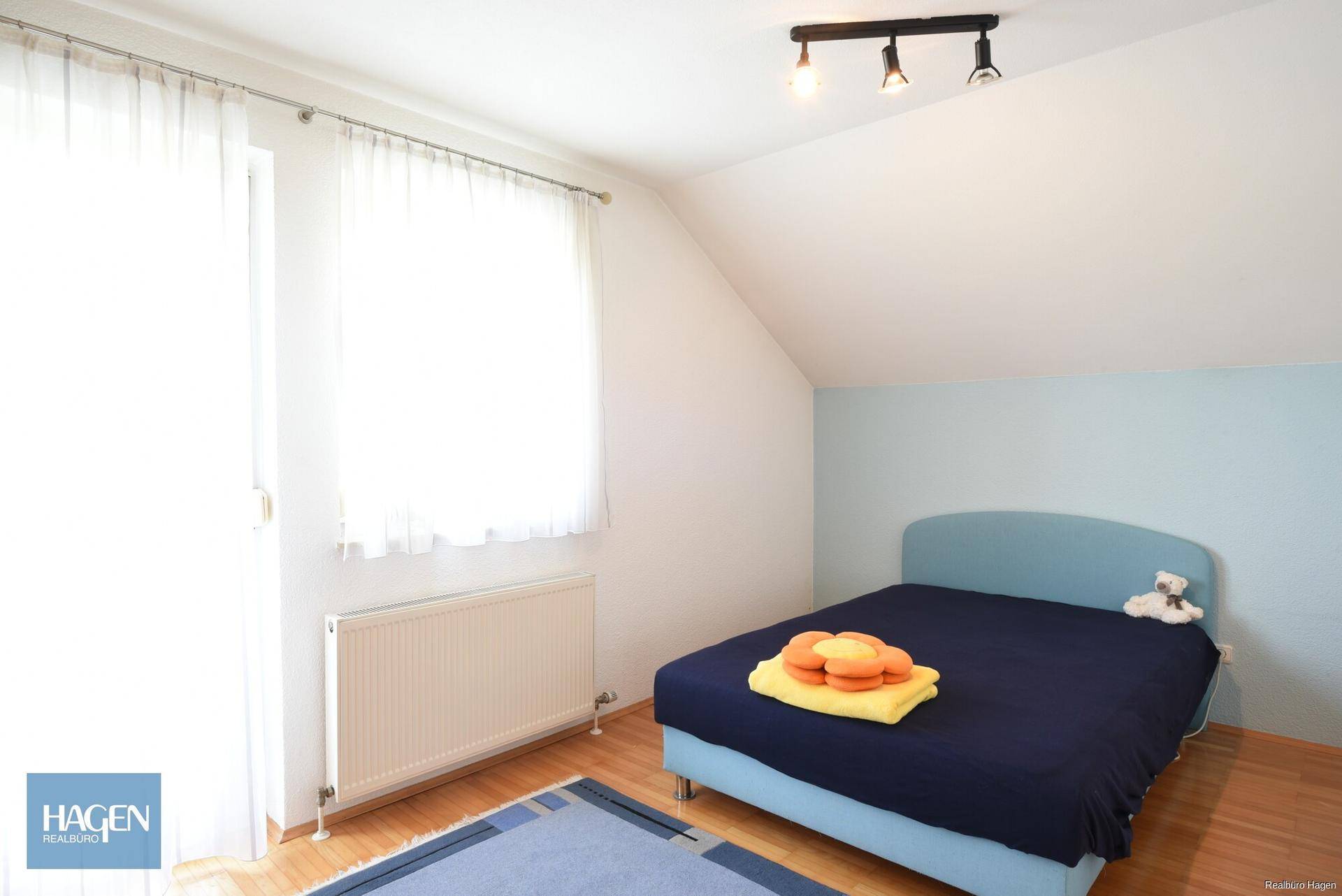 Kinderzimmer mit Dachschräge, Holzboden, blauer Akzentwand und hellem Fenster.