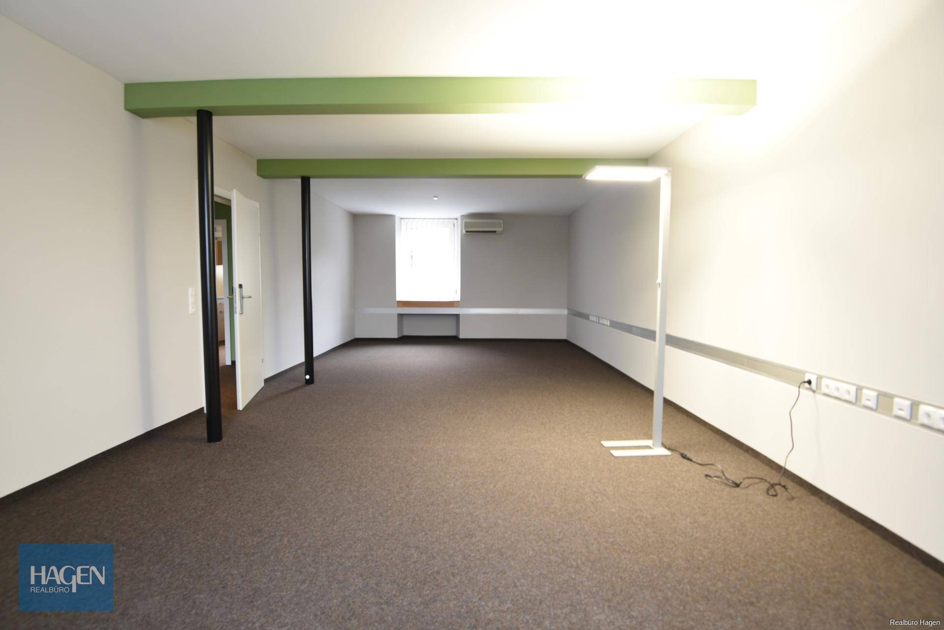 Großes, leeres Büro mit Teppichboden, weißen Wänden und sichtbaren grünen Trägern.