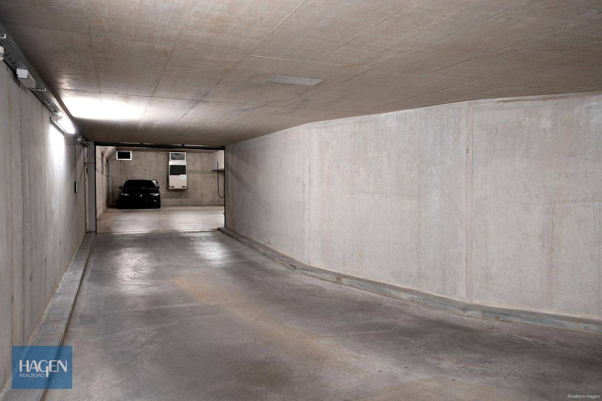 Tiefgarageneinfahrt mit Betonwänden und -decke, die zu den Parkplätzen führt.